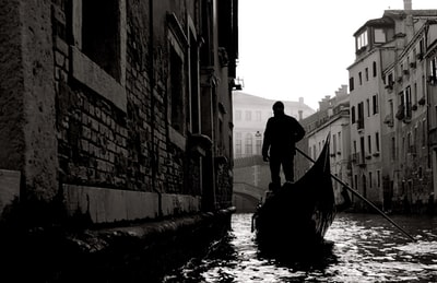 一个穿着黑色夹克和蓝色牛仔牛仔裤的男人白天站在河边的船上